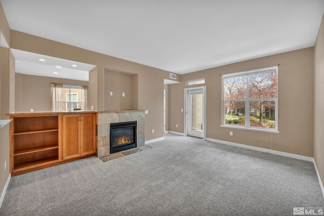 unfurnished living room with a fireplace, visible vents, a healthy amount of sunlight, light carpet, and baseboards