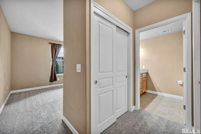 hall with baseboards, visible vents, and light colored carpet