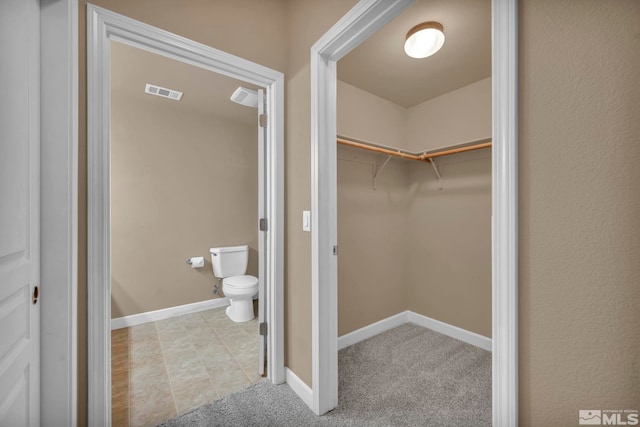 bathroom with baseboards, visible vents, a spacious closet, and toilet