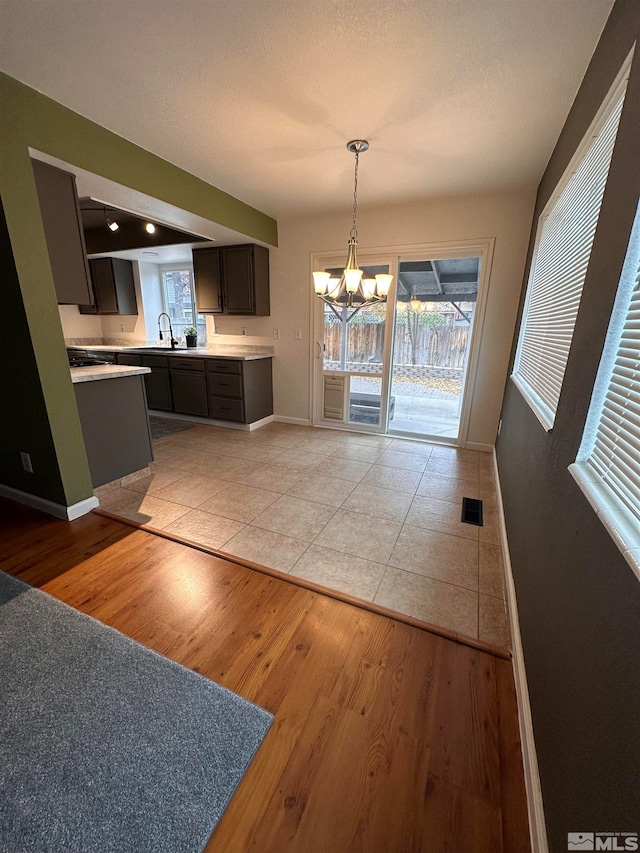 kitchen featuring dark brown cabinetry, sink, a chandelier, decorative light fixtures, and light wood-type flooring