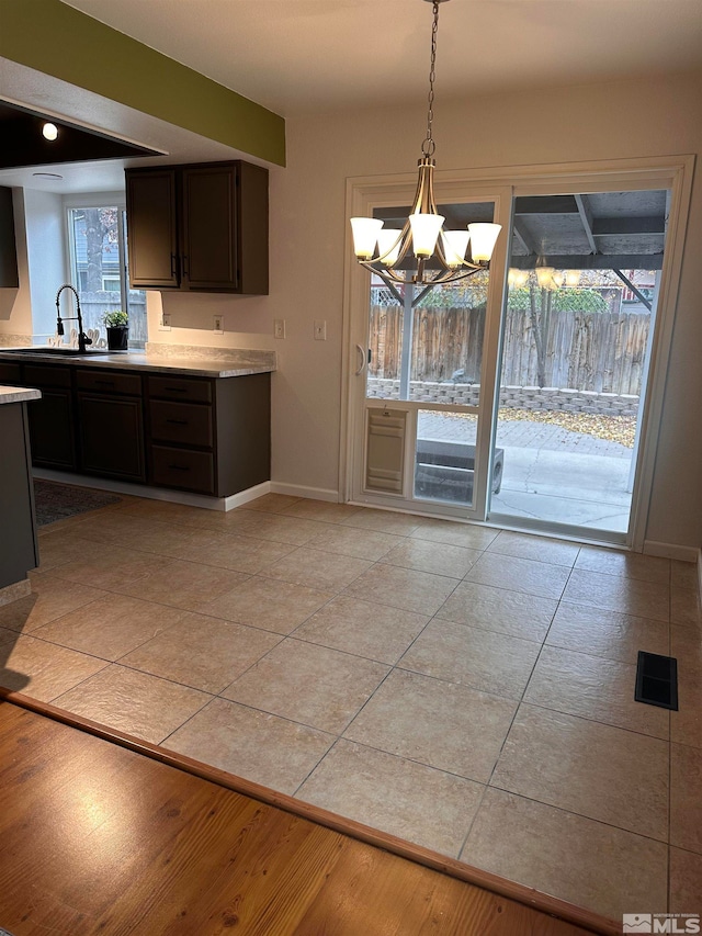 kitchen featuring sink, hanging light fixtures, an inviting chandelier, dark brown cabinets, and light tile patterned floors