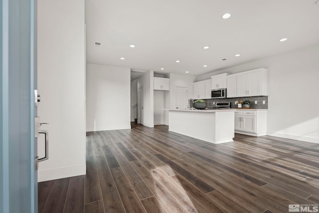 kitchen featuring a kitchen island with sink, dark hardwood / wood-style flooring, decorative backsplash, white cabinets, and appliances with stainless steel finishes