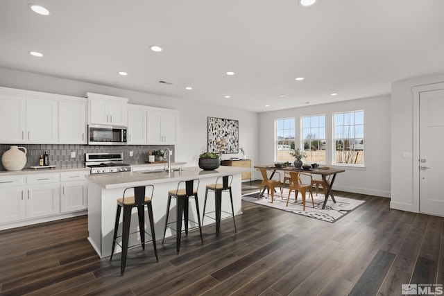 kitchen featuring stainless steel appliances, white cabinetry, dark wood-type flooring, and a center island with sink