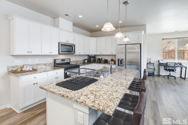 kitchen featuring hanging light fixtures, light hardwood / wood-style flooring, an island with sink, white cabinets, and appliances with stainless steel finishes