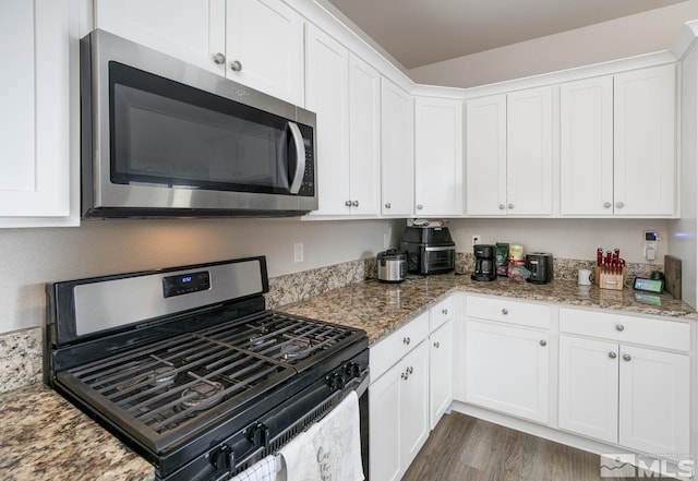 kitchen featuring light stone countertops, dark hardwood / wood-style flooring, stainless steel appliances, and white cabinetry