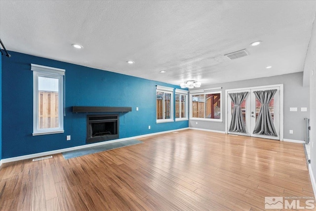 unfurnished living room with french doors, a textured ceiling, and light hardwood / wood-style flooring