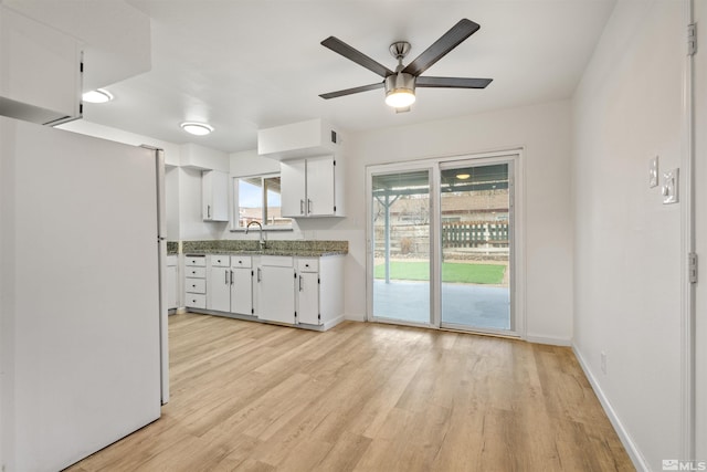 kitchen featuring light wood-type flooring, ceiling fan, sink, white refrigerator, and white cabinetry