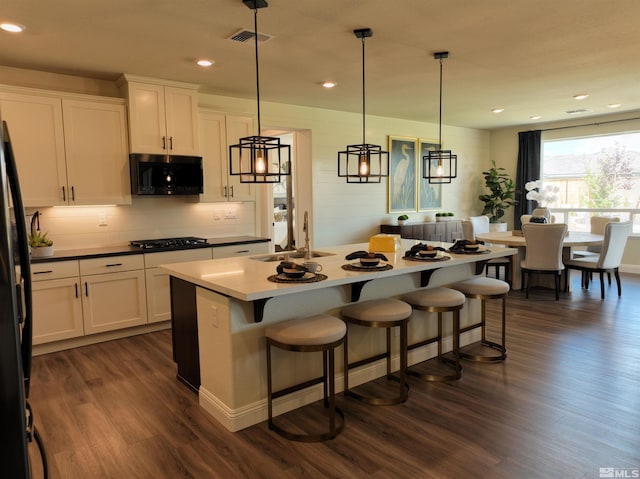 kitchen with dark hardwood / wood-style flooring, black appliances, sink, a center island with sink, and hanging light fixtures