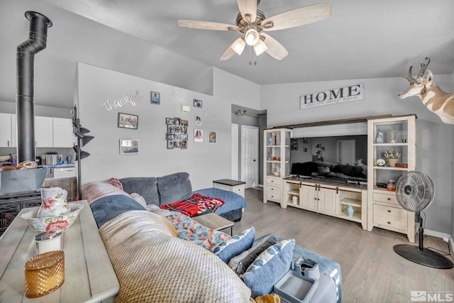 living room featuring hardwood / wood-style floors, ceiling fan, a wood stove, and vaulted ceiling