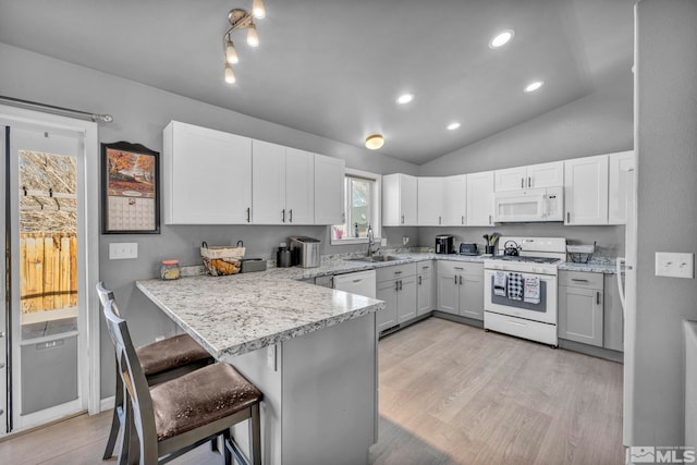 kitchen with lofted ceiling, white appliances, kitchen peninsula, white cabinetry, and a breakfast bar area