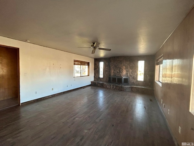 unfurnished living room with a fireplace, ceiling fan, dark wood-type flooring, and a healthy amount of sunlight