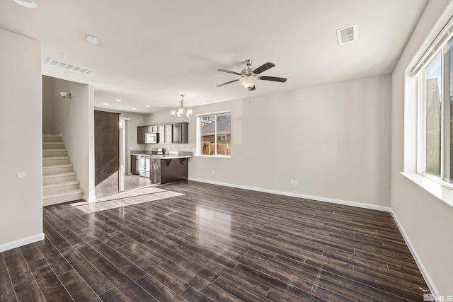 unfurnished living room featuring ceiling fan with notable chandelier and dark hardwood / wood-style flooring