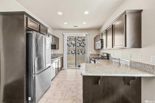 kitchen with a kitchen breakfast bar, light stone countertops, appliances with stainless steel finishes, light tile patterned flooring, and kitchen peninsula