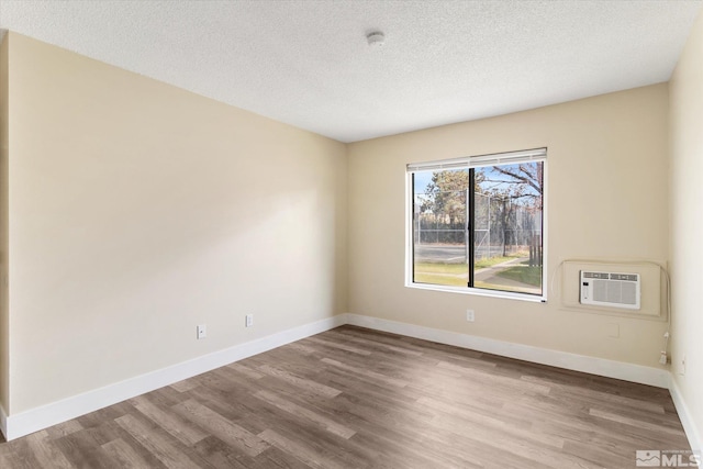 empty room featuring an AC wall unit, light hardwood / wood-style floors, and a textured ceiling