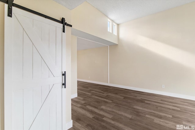 unfurnished room with dark hardwood / wood-style floors, a barn door, and a textured ceiling