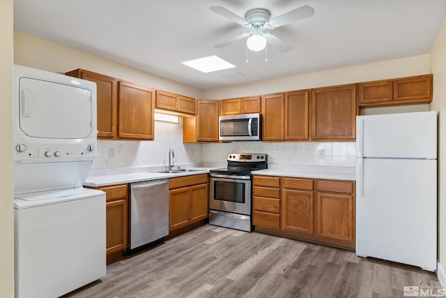 kitchen with light wood-type flooring, stainless steel appliances, ceiling fan, sink, and stacked washer and dryer