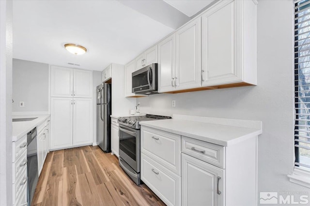 kitchen with plenty of natural light, white cabinets, light hardwood / wood-style flooring, and appliances with stainless steel finishes