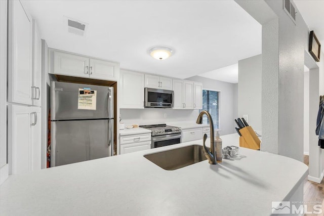 kitchen featuring kitchen peninsula, white cabinetry, light hardwood / wood-style flooring, and appliances with stainless steel finishes