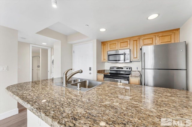 kitchen with sink, stacked washing maching and dryer, light hardwood / wood-style floors, light stone counters, and stainless steel appliances