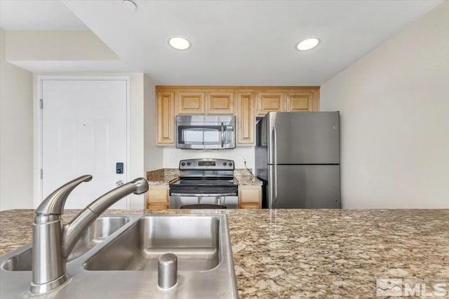 kitchen with stone counters, appliances with stainless steel finishes, light brown cabinetry, and sink