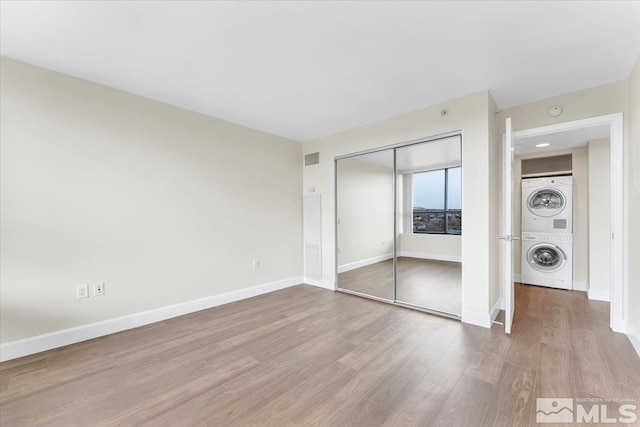 unfurnished bedroom featuring light wood-type flooring, stacked washing maching and dryer, and a closet