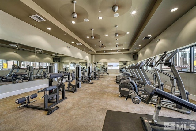 workout area featuring a high ceiling, light colored carpet, a raised ceiling, and ceiling fan