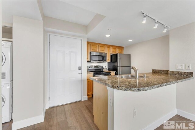 kitchen featuring kitchen peninsula, appliances with stainless steel finishes, light wood-type flooring, sink, and stacked washer and dryer