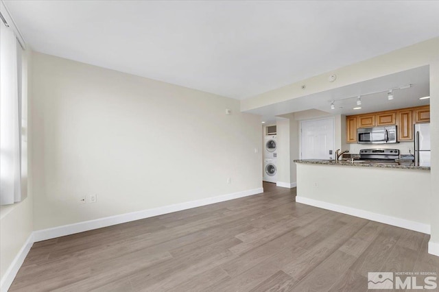 unfurnished living room featuring rail lighting, light hardwood / wood-style floors, stacked washer and clothes dryer, and sink