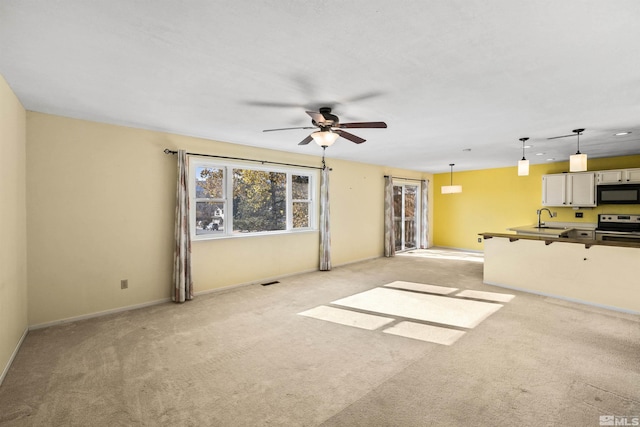 unfurnished living room featuring light carpet, sink, and ceiling fan