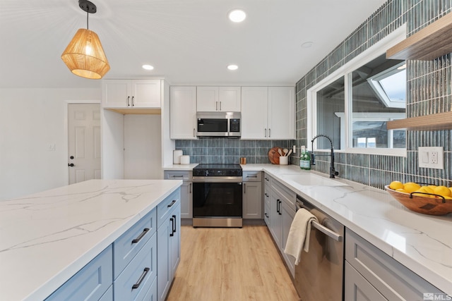 kitchen featuring light wood-type flooring, stainless steel appliances, sink, decorative light fixtures, and white cabinetry