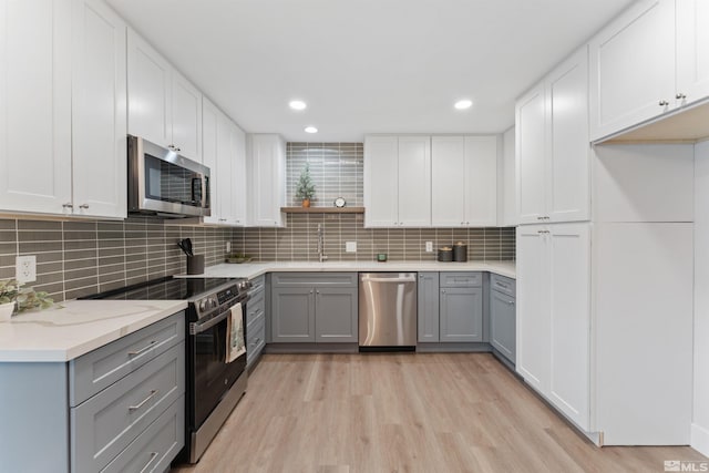 kitchen featuring light wood-type flooring, tasteful backsplash, stainless steel appliances, gray cabinets, and white cabinetry