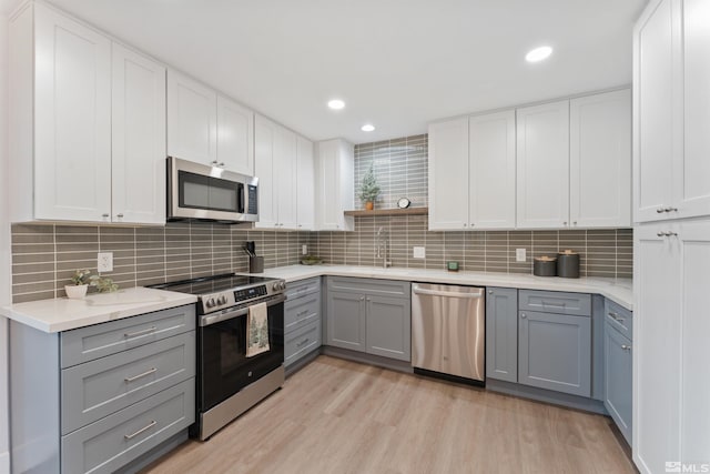 kitchen featuring gray cabinetry, white cabinets, light wood-type flooring, and stainless steel appliances