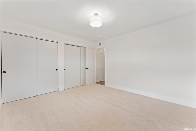 unfurnished bedroom with light carpet and multiple closets