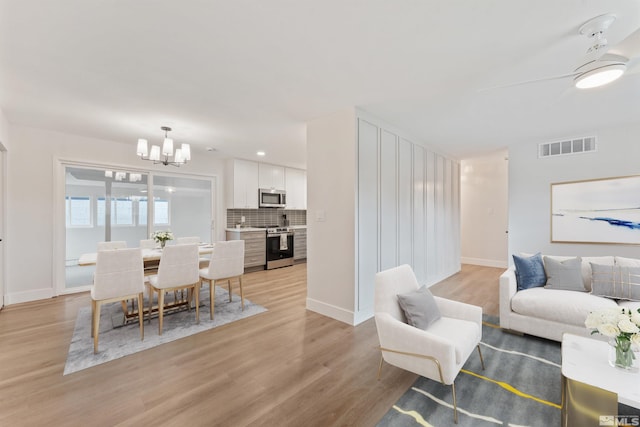 living room featuring ceiling fan with notable chandelier and light hardwood / wood-style flooring