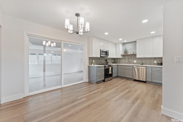 kitchen with gray cabinetry, hanging light fixtures, stainless steel appliances, decorative backsplash, and light wood-type flooring