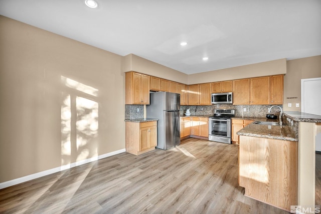 kitchen with backsplash, stone counters, sink, light wood-type flooring, and stainless steel appliances