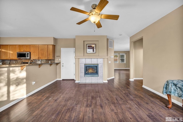 unfurnished living room with a fireplace, ceiling fan, dark hardwood / wood-style flooring, and sink