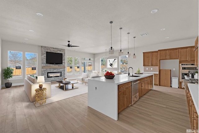 kitchen featuring ceiling fan, sink, stainless steel appliances, a stone fireplace, and an island with sink