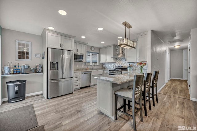 kitchen with pendant lighting, stainless steel appliances, wall chimney range hood, and light hardwood / wood-style flooring