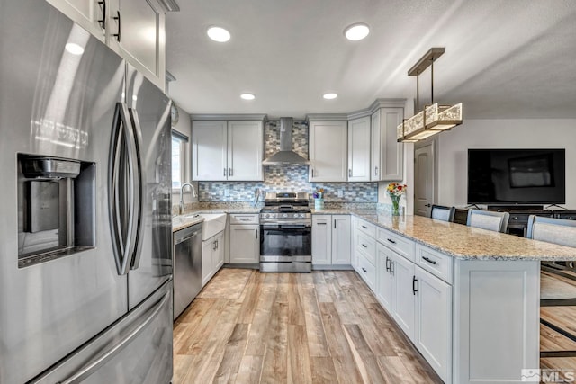 kitchen with a breakfast bar, wall chimney range hood, decorative light fixtures, kitchen peninsula, and stainless steel appliances