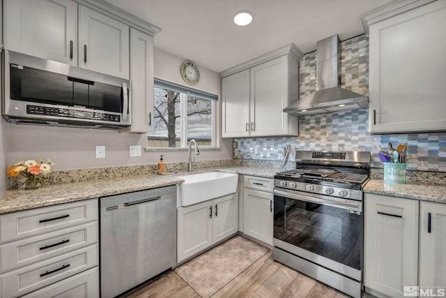 kitchen featuring wall chimney exhaust hood, stainless steel appliances, sink, light hardwood / wood-style flooring, and white cabinets