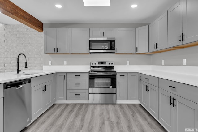 kitchen featuring gray cabinetry, stainless steel appliances, sink, light hardwood / wood-style flooring, and beamed ceiling