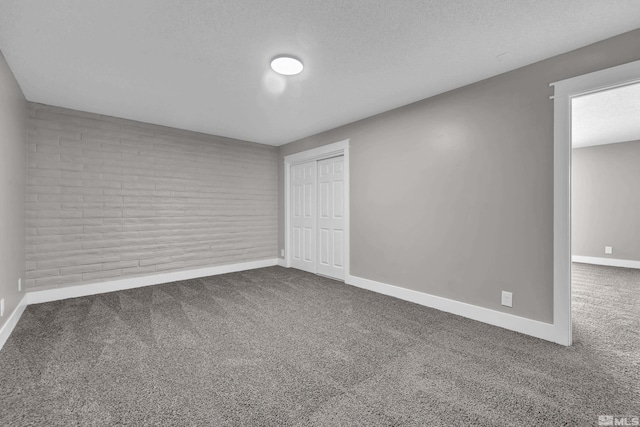 unfurnished room with carpet, a textured ceiling, and brick wall