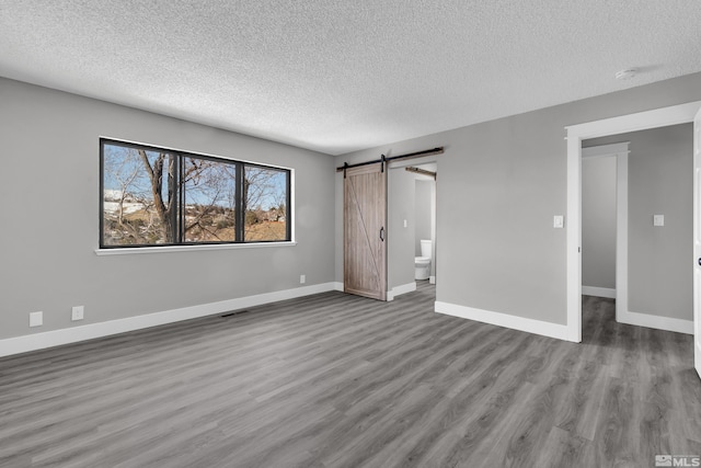 unfurnished bedroom with a textured ceiling, a barn door, hardwood / wood-style flooring, and ensuite bathroom