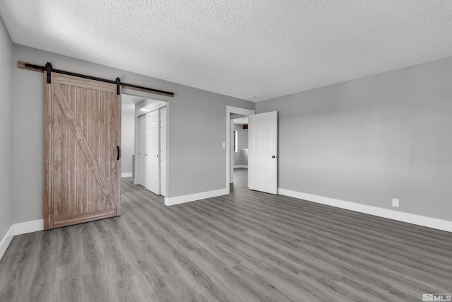 unfurnished bedroom with a barn door, a textured ceiling, a closet, and light hardwood / wood-style flooring