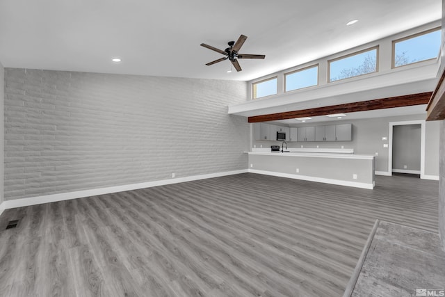 unfurnished living room featuring high vaulted ceiling, ceiling fan, dark wood-type flooring, and brick wall