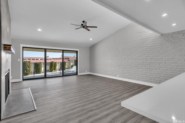 unfurnished living room with ceiling fan, hardwood / wood-style floors, high vaulted ceiling, and brick wall