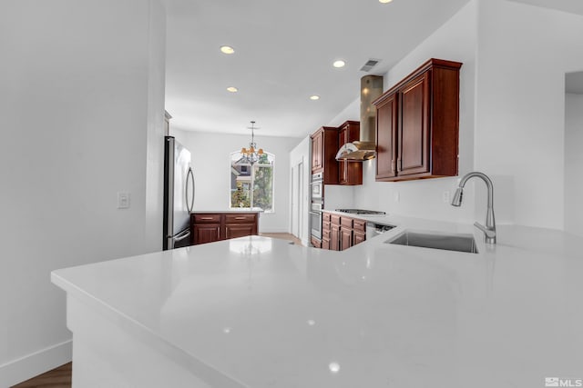 kitchen featuring wall chimney range hood, sink, decorative light fixtures, kitchen peninsula, and stainless steel appliances