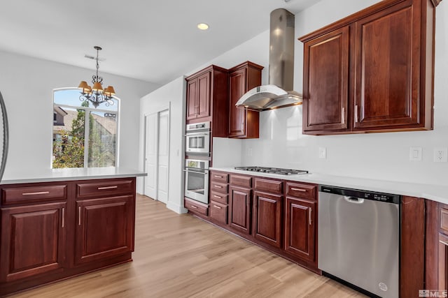 kitchen featuring wall chimney exhaust hood, stainless steel appliances, a notable chandelier, decorative light fixtures, and light wood-type flooring