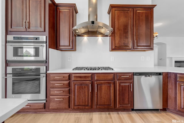 kitchen with stainless steel appliances, wall chimney exhaust hood, and light hardwood / wood-style floors